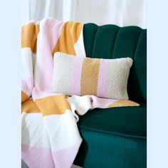 a green couch with a pink and yellow striped blanket on it's back next to a pillow