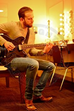 a man sitting on a chair playing an electric guitar