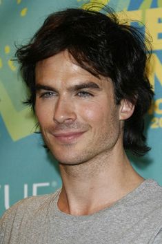 a close up of a person wearing a gray shirt and smiling at the camera with his hair pulled back