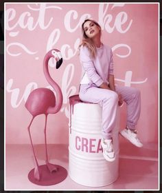 a woman sitting on top of a white barrel next to a pink flamingo wall