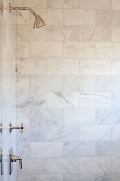 a bathroom with white marble walls and floor, shower head and hand held faucet