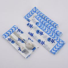 three napkins with blue and white designs on them are next to a fork and knife