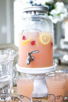 a pitcher filled with pink lemonade sitting on top of a table next to glasses