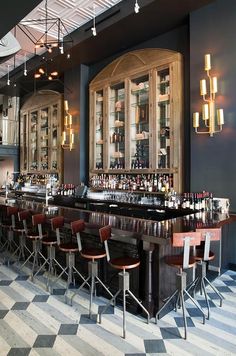 an empty bar with many chairs and bottles on the back wall, in front of a checkered floor