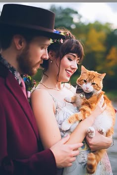 a woman holding a cat while standing next to a man in a top hat and dress