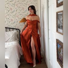 a woman in an orange dress standing next to a bed and looking at the camera