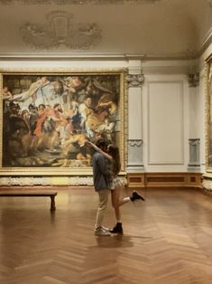 two people standing in front of a large painting on the wall and wooden flooring