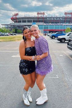 two women in short dresses standing next to each other on a parking lot near a stadium