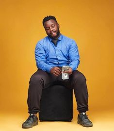 a man sitting on top of a stool with money in his hand and smiling at the camera