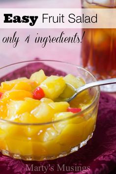 a glass bowl filled with fruit salad on top of a purple cloth next to a cup of tea