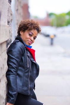 a woman leaning against a brick wall wearing a black leather jacket and leggings