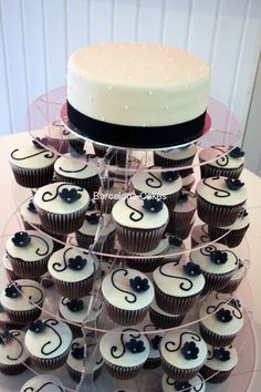 a cake and cupcakes are arranged on a clear display stand with black ribbon