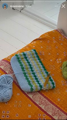 a crochet bag sitting on top of a bed next to balls of yarn