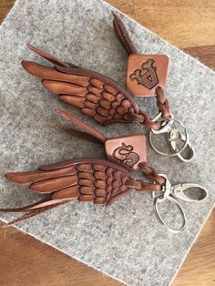 two leather key chains with angel wings on them sitting on top of a piece of cloth