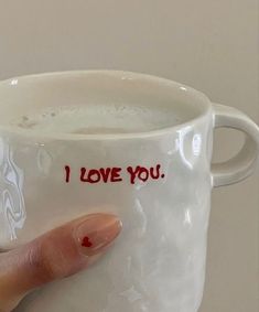 a hand holding a coffee mug with i love you written on the inside and red writing on the outside