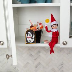 an elf is sitting on the shelf with candy in front of him and holding a lollipop