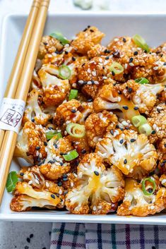 sweet and spicy baked cauliflower with sesame seeds in a white square dish, with chopsticks on the side