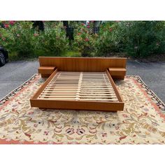 a wooden bed frame sitting on top of a rug in the middle of a driveway