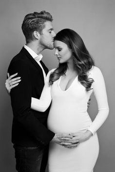 a pregnant couple kissing while standing next to each other