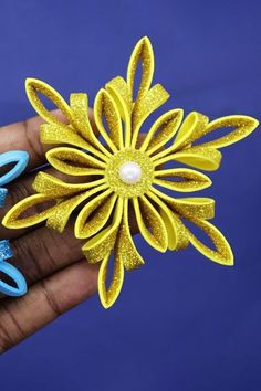 a person holding two yellow and blue hair clips in their hand, one with a flower on it