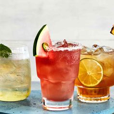 three different types of drinks are lined up on a table with limes and watermelon