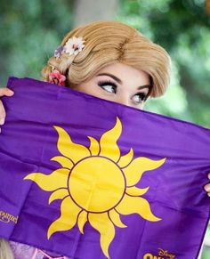 a woman holding up a purple and yellow flag with the sun on it's side