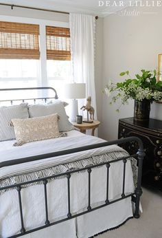 a bed with white sheets and pillows in a bedroom next to a dresser, lamp and window