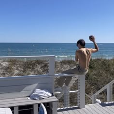 a man sitting on a bench looking out at the ocean with his arm in the air