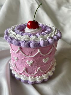 a pink and purple cake sitting on top of a white cloth covered table next to a cherry