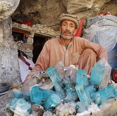 a man sitting in front of a pile of rocks and ice cubes on the ground