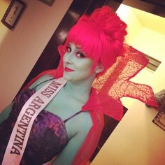 a woman with red hair and makeup wearing a sash