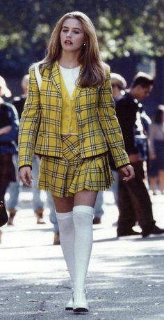 a woman walking down the street wearing a yellow jacket and short skirt with thigh high socks