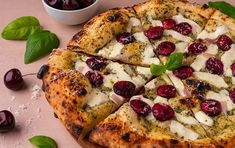 a pizza sitting on top of a wooden cutting board next to a bowl of cherries