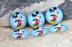 five mickey mouse buttons sitting on top of a rock next to a rock with a stone in the background