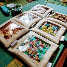 four square pieces of fabric with buttons on them sitting on top of a cutting board