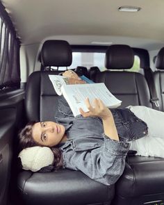 a woman laying on the back of a car reading a book