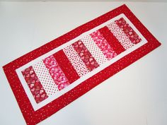 a red and white patchwork table runner with hearts on the border, sitting on a white surface