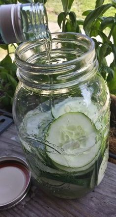 a mason jar filled with cucumber slices next to a cup of liquid on top of a wooden table