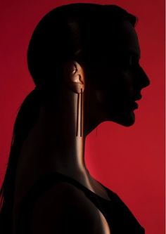 a woman's profile with earrings in the shape of her head and neck, against a red background