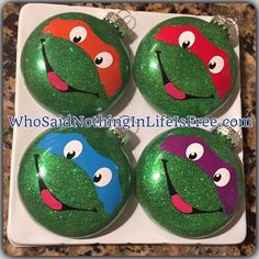 four teenage mutant turtle ornaments on a white plate with green and red glitter paint,