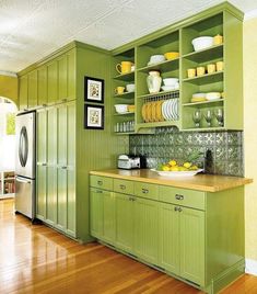 a kitchen with green cabinets and yellow plates on the counter top, along with wooden floors