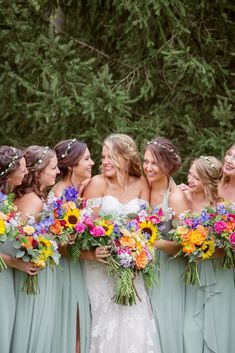 a group of women standing next to each other in front of some trees and holding bouquets