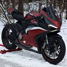 a red and black motorcycle parked on the side of a snow covered road next to trees