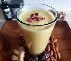 a glass filled with liquid sitting on top of a wooden table next to nuts and flowers