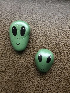 two green rocks with faces painted on them sitting on a brown leather surface next to each other