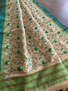 Gorgeous cotton tissue saree in soothing beige color. Colorful floral embroidery all over the saree is simply eye catching. Teal and light green border and anchal gives an elegant look. Comes with a separate blouse piece with saree border (7th pic). Suitable to wear in an afternoon party. Saree is 5.5+ yards and 43 inches wide Blouse piece is 31.5 inches Care: Dry clean only Disclaimer: Color and shade of saree may vary in the pictures than the actual item. There might be slight weaving irregula Pista Green Cotton Silk Saree With Resham Embroidery, Green Embroidered Cotton Silk Dupatta, Beige Zari Work Tissue Silk Saree, Beige Tissue Silk Saree With Zari Work, Semi-stitched Chanderi Saree In Beige, Semi-stitched Beige Chanderi Saree, Beige Semi-stitched Chanderi Saree, Embroidered Cream Chanderi Saree, Embroidered Beige Saree In Traditional Drape