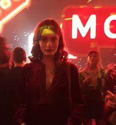 a woman standing in front of a neon sign at a party with other people around her