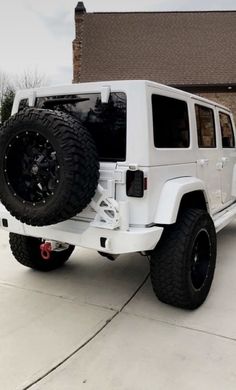 a white jeep is parked in front of a brick building with large tires on it