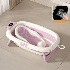 a pink and white baby bath tub sitting on top of a floor next to a digital thermometer