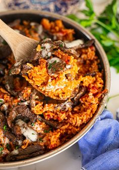 a pot filled with meat and rice on top of a table next to a wooden spoon